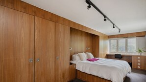 Quarto com cama, guarda-roupa de madeira, escrivaninha e janela.