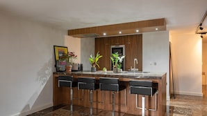 Cozinha moderna com ilha central, banquetas e plantas em vasos.