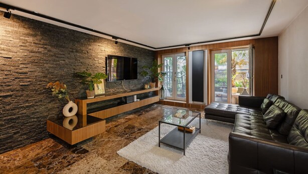 Uma sala de estar moderna com parede de pedra, TV de tela plana, sofá de couro e mesa de centro de vidro.