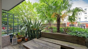 Varanda com bancos de madeira, plantas em vasos e vista para um edifício com uma placa que diz 'CHIC'.