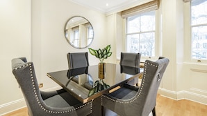 A dining room with a glass table, four upholstered chairs, a round mirror, and a potted plant. - Luxury Knightsbridge Home Next To Hyde Park (London)