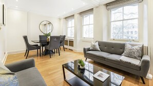 A modern living room with a grey sofa, a coffee table, and a dining area with a table and chairs. - Luxury Knightsbridge Home Next To Hyde Park (London)