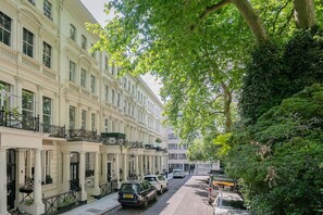 Eine Reihe traditioneller europäischer Stadthäuser mit Balkonen, parkgeparkten Autos und einer von Bäumen gesäumten Straße.