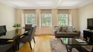 A spacious living room with a dining area, large windows, a sofa, and a TV. - Luxury Knightsbridge Home Next To Hyde Park (London)