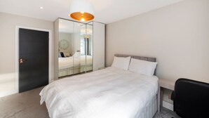 A modern bedroom with a large bed, a mirror, a door, and a ceiling light. - Best Location in London 3-bed Chelsea Home (London)