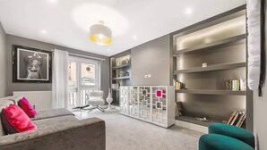 A modern living room with a grey sofa, teal armchairs, a white decorative partition, and a bookshelf. - Best Location in London 3-bed Chelsea Home (London)