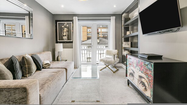 A modern living room with a sofa, a glass coffee table, a white armchair, a TV, and a bookshelf. - Best Location in London 3-bed Chelsea Home (London)