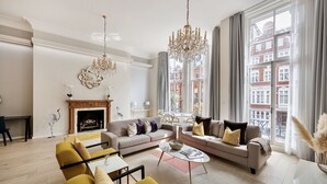 Amplia sala de estar con chimenea, un candelabro y ventanas grandes con vistas a la ciudad.