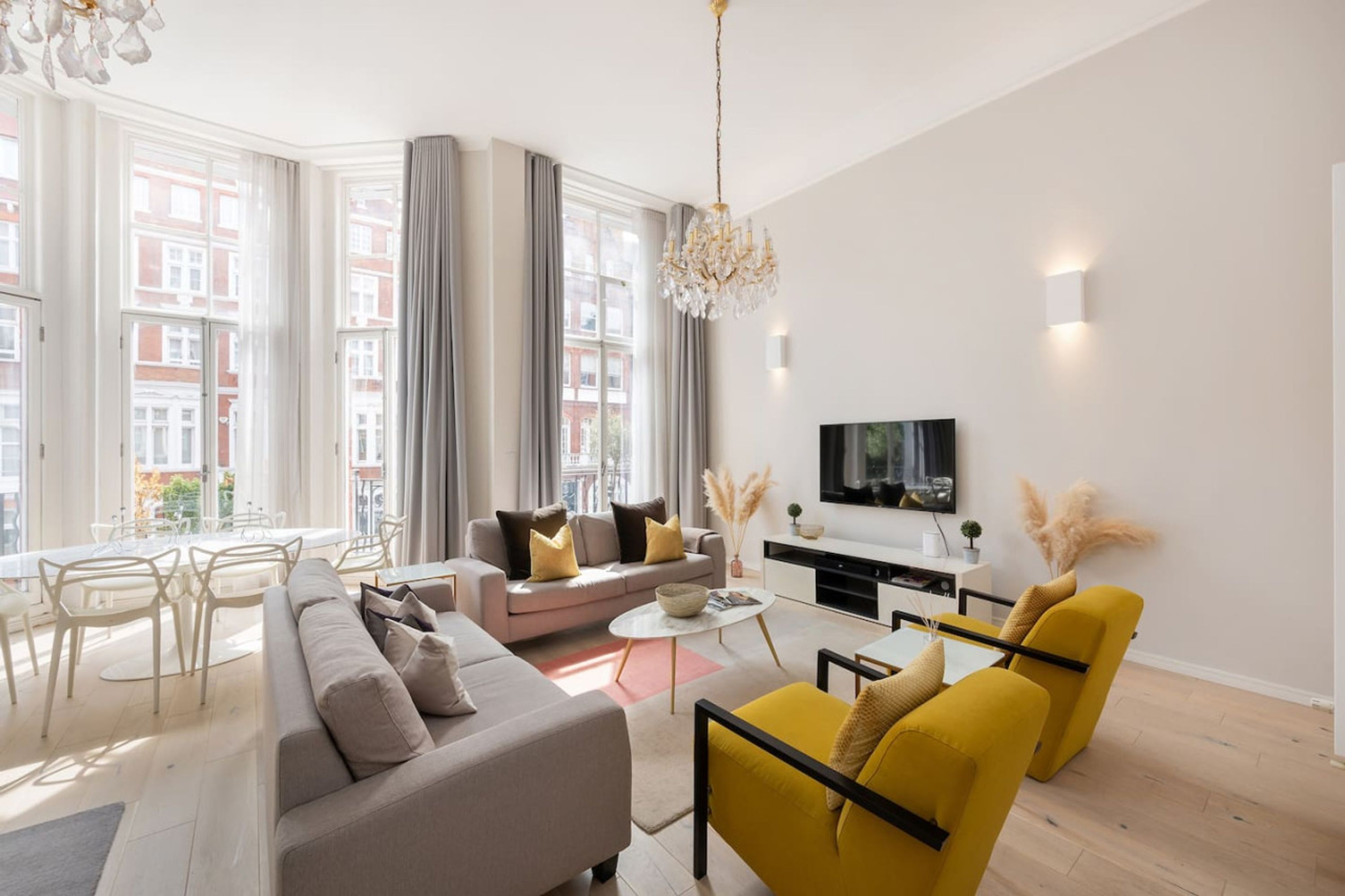 A modern living room with a sofa, yellow armchairs, a dining area, and a TV mounted on the wall.