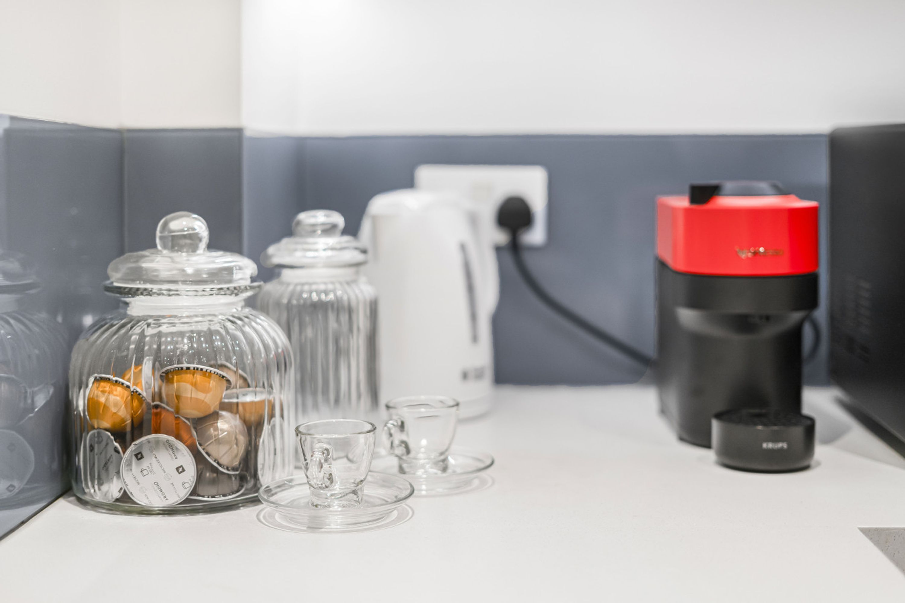 A kitchen counter with a coffee maker, a kettle, and a glass jar with tea bags.
