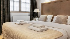 A neatly made bed with folded towels, a bedside lamp, and a window with curtains. - Stylish Hyde Park 2-bed Step-free Pet Friendly (London)