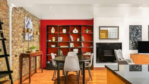 A modern kitchen with a red accent wall, a brick wall, and a dining area with a round table and chairs. - Stylish Hyde Park 2-bed Step-free Pet Friendly (London)