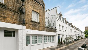 A row of white terraced houses with brick facades, a clear sky, and a person sitting on a bench. - Stylish Hyde Park 2-bed Step-free Pet Friendly (London)