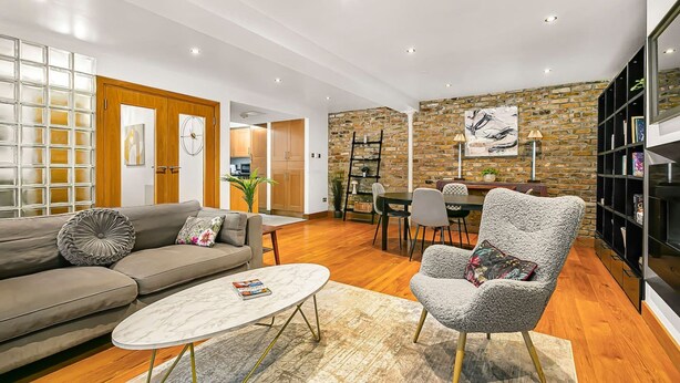 A modern living room with a sofa, armchair, coffee table, and a dining area with chairs and a table. - Stylish Hyde Park 2-bed Step-free Pet Friendly (London)