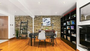 A dining area with a brick wall, wooden flooring, a round table, and chairs. - Stylish Hyde Park 2-bed Step-free Pet Friendly (London)
