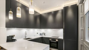 A modern kitchen with dark cabinetry, a white marble island, stainless steel appliances, and pendant lighting. - Ultra Luxury Holland Park Home - Central AC (London)