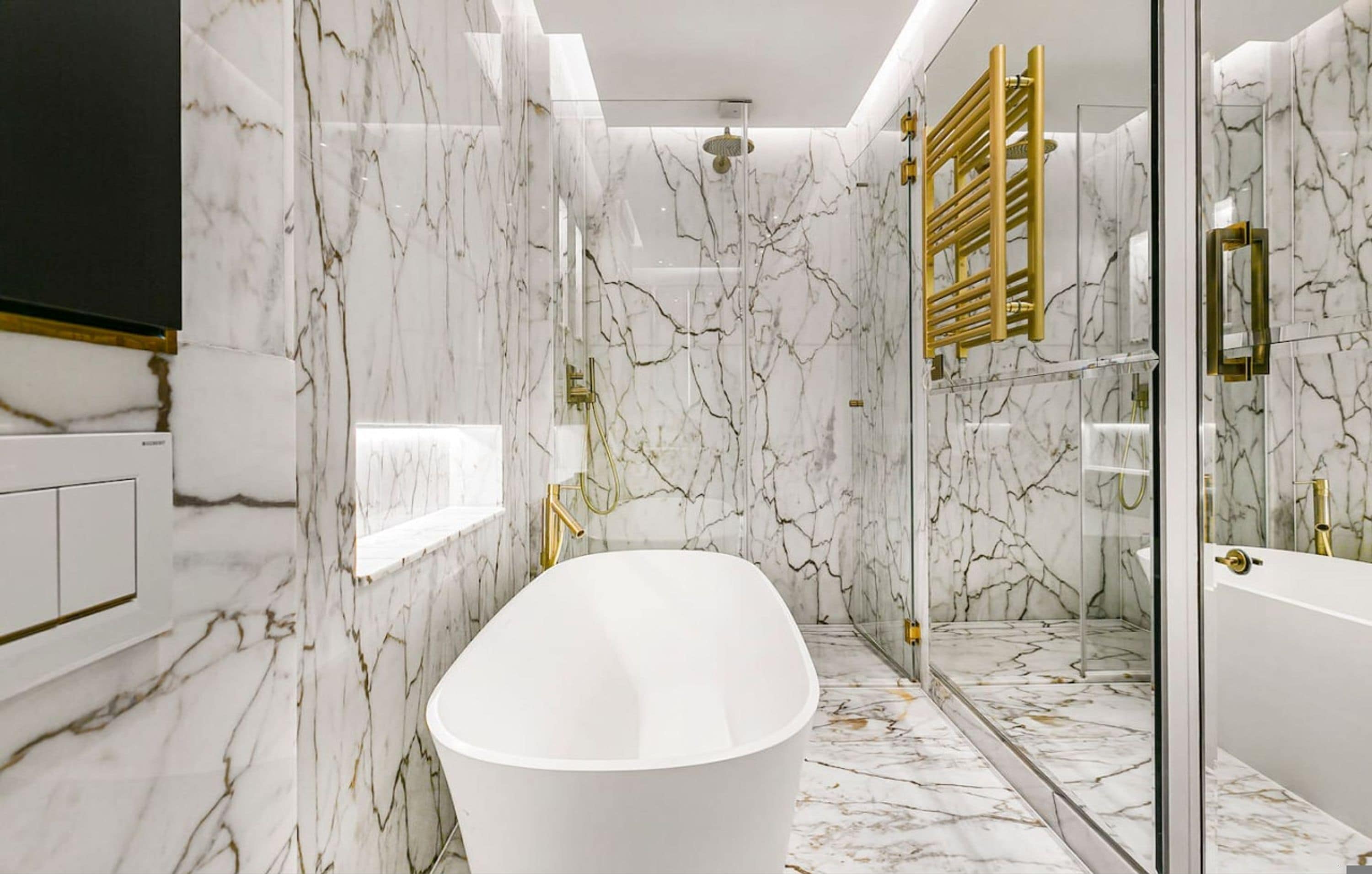 A modern bathroom with a freestanding bathtub, marble walls, and gold fixtures.