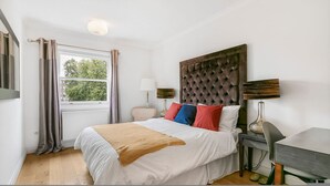 Una camera da letto con un letto grande, una testiera, due abat-jour, un comodino, una finestra con tende e una scrivania con una sedia.