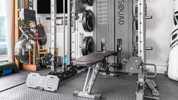 A gym with weightlifting equipment, a bench, and a wall-mounted weight rack. - 4-bed Knightsbridge Home Gym Cinema Jacuzzi (London)