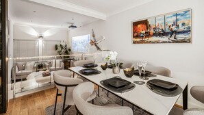 A modern dining area with a long table set for six, surrounded by comfortable chairs. A cityscape is visible through the window, and a painting adorns the wall. - 4-bed Knightsbridge Home Gym Cinema Jacuzzi (London)