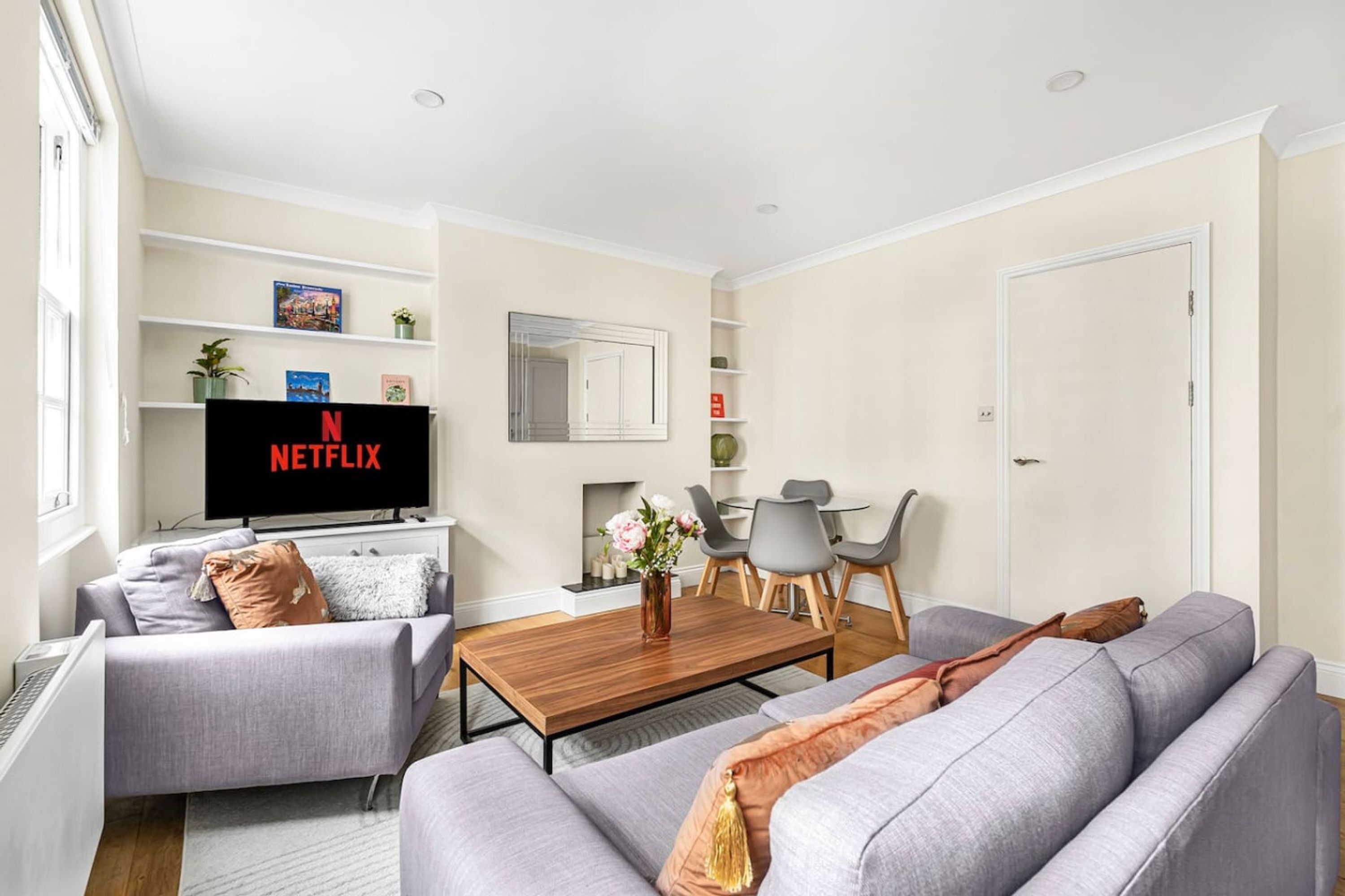 Una sala de estar moderna con un televisor de pantalla plana, sofás grises, una mesa de centro de madera y un comedor con sillas y una mesa pequeña.