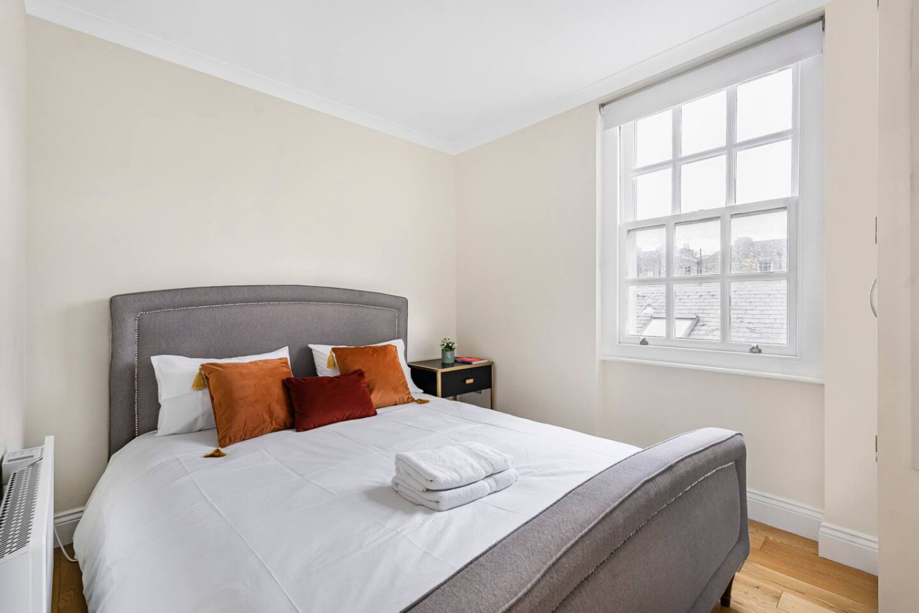 A neatly arranged bedroom with a large bed, a nightstand, and a window with a view.