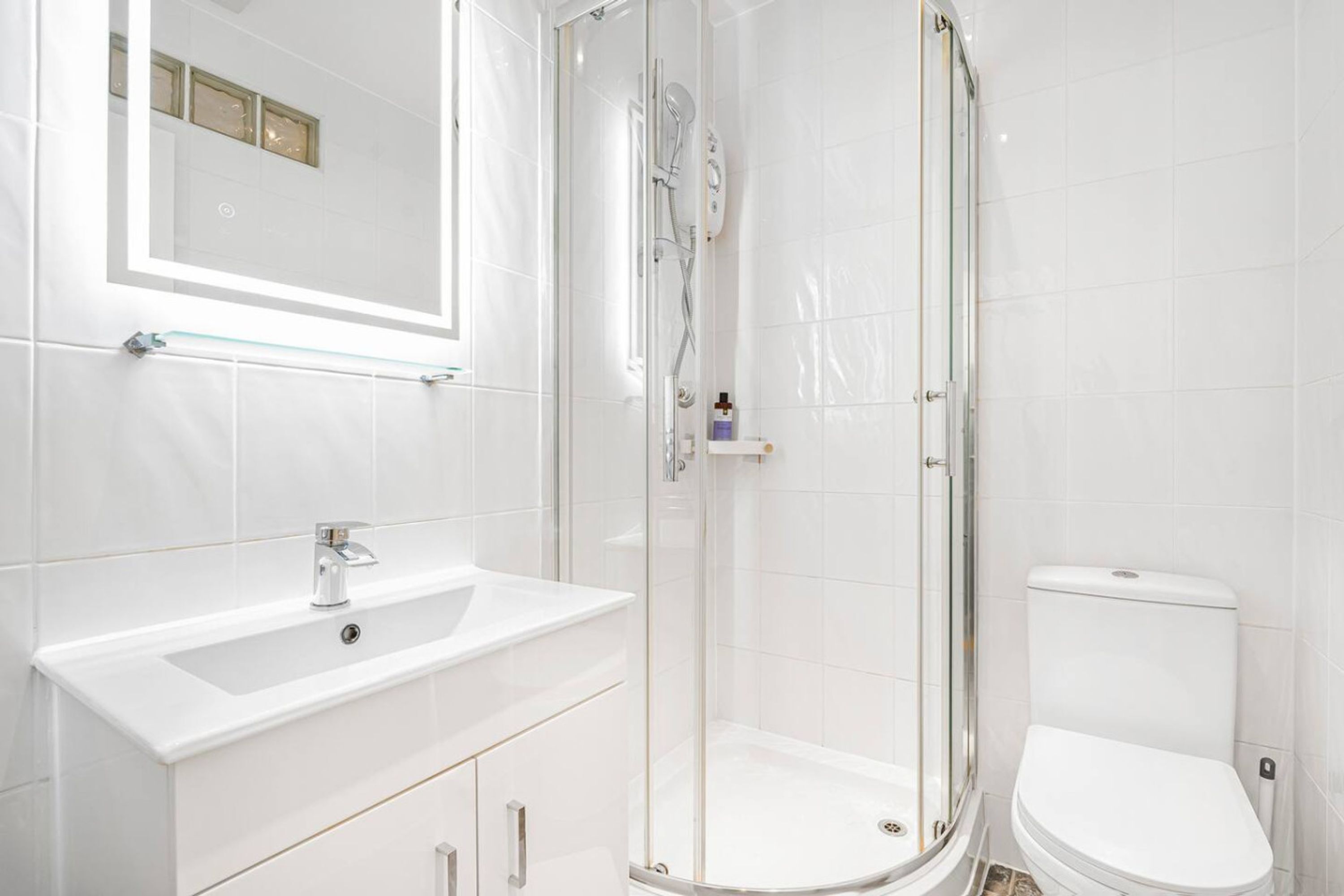 A bathroom with a glass-enclosed shower, a white sink, and a toilet.