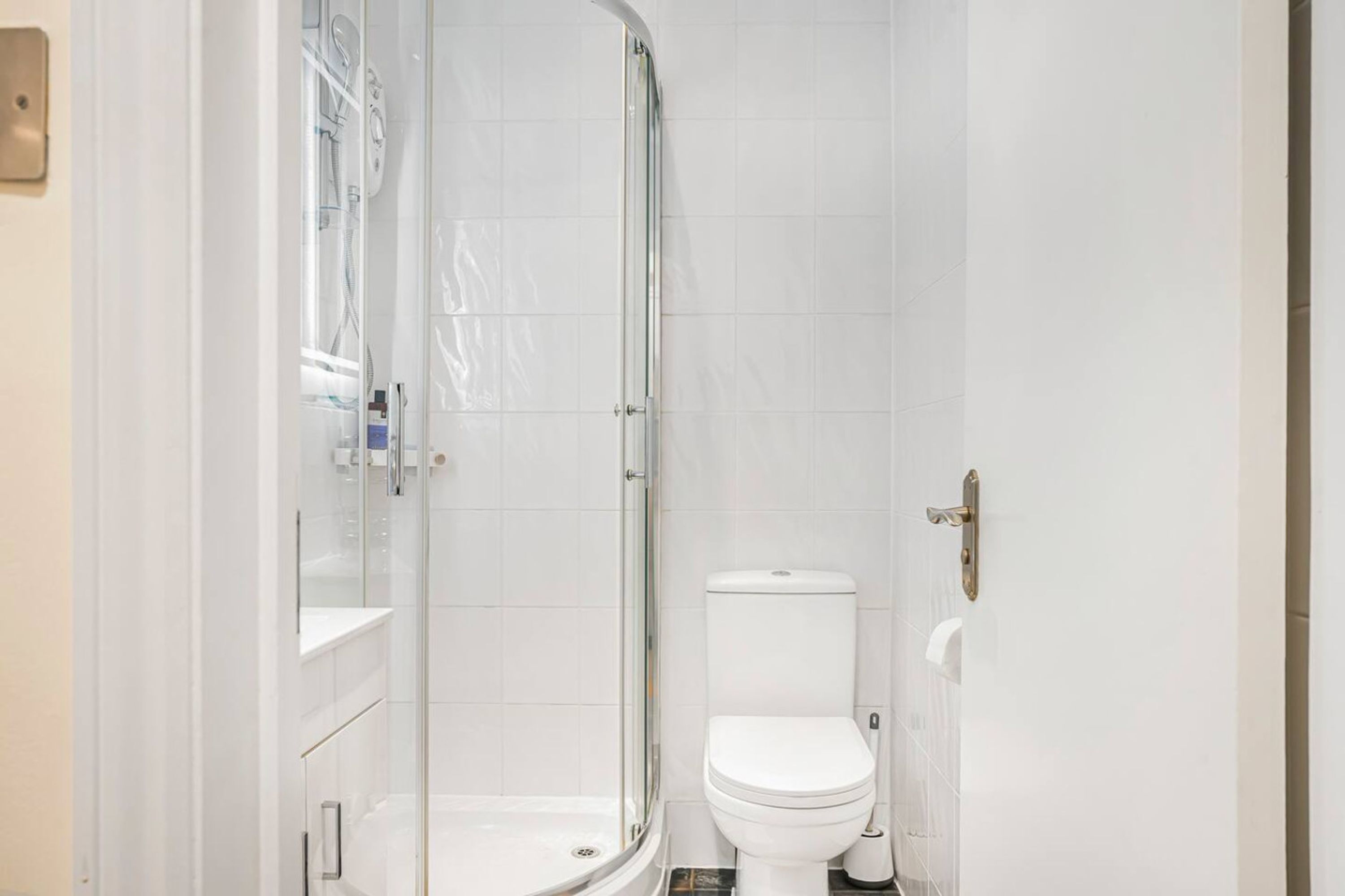Un baño moderno con ducha envuelta en vidrio, inodoro blanco y lavamanos blanco.