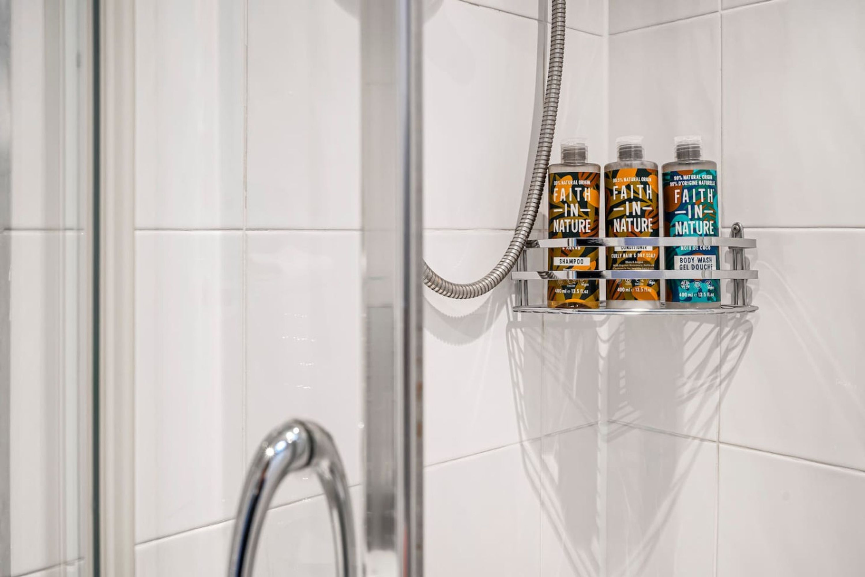 A shower area with a glass shelf holding three bottles of shampoo and body wash.