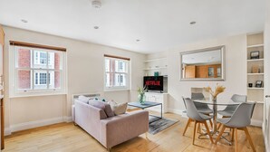 Una sala moderna con un sofá, una mesa de centro y un comedor con sillas, y un televisor mostrando 'NETFLIX'.