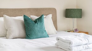 Una cama bien hecha con ropa blanca y una almohada verde azulada.