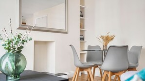 Un comedor moderno con una mesa de vidrio, sillas grises y un jarrón verde con ramas.