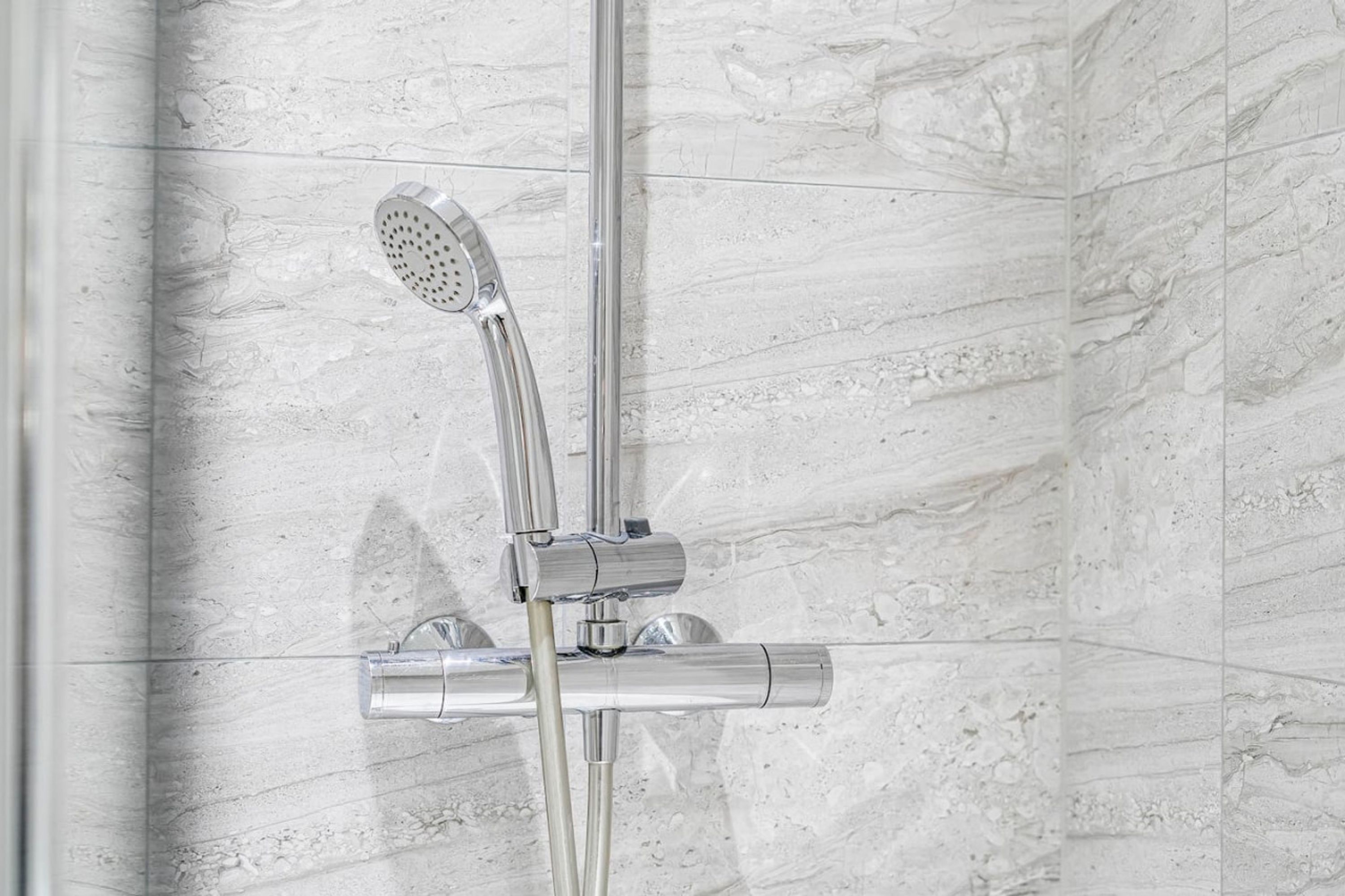 Eine moderne Dusche mit Handbrause und ein an der Wand montiertem Wasserhahn.