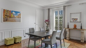 A dining area with a dark wooden table, grey upholstered chairs, a colorful rug, and a painting of a street scene on the wall. - Luxury 4 Bed Residence - Next to Arc de Triomphe (Paris)