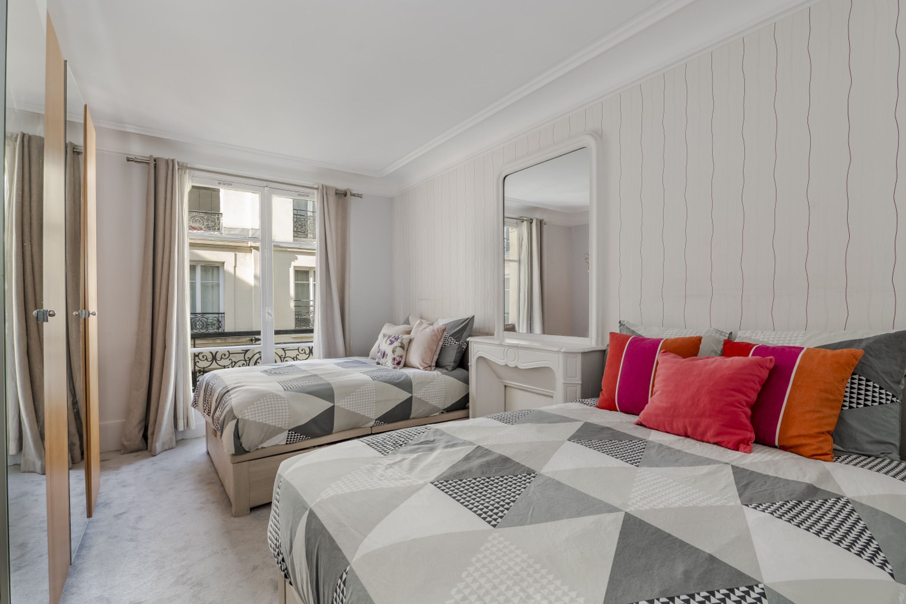 Ein Schlafzimmer mit einem Bett, einem Schminktisch, einem Spiegel und einem Fenster mit Vorhängen.