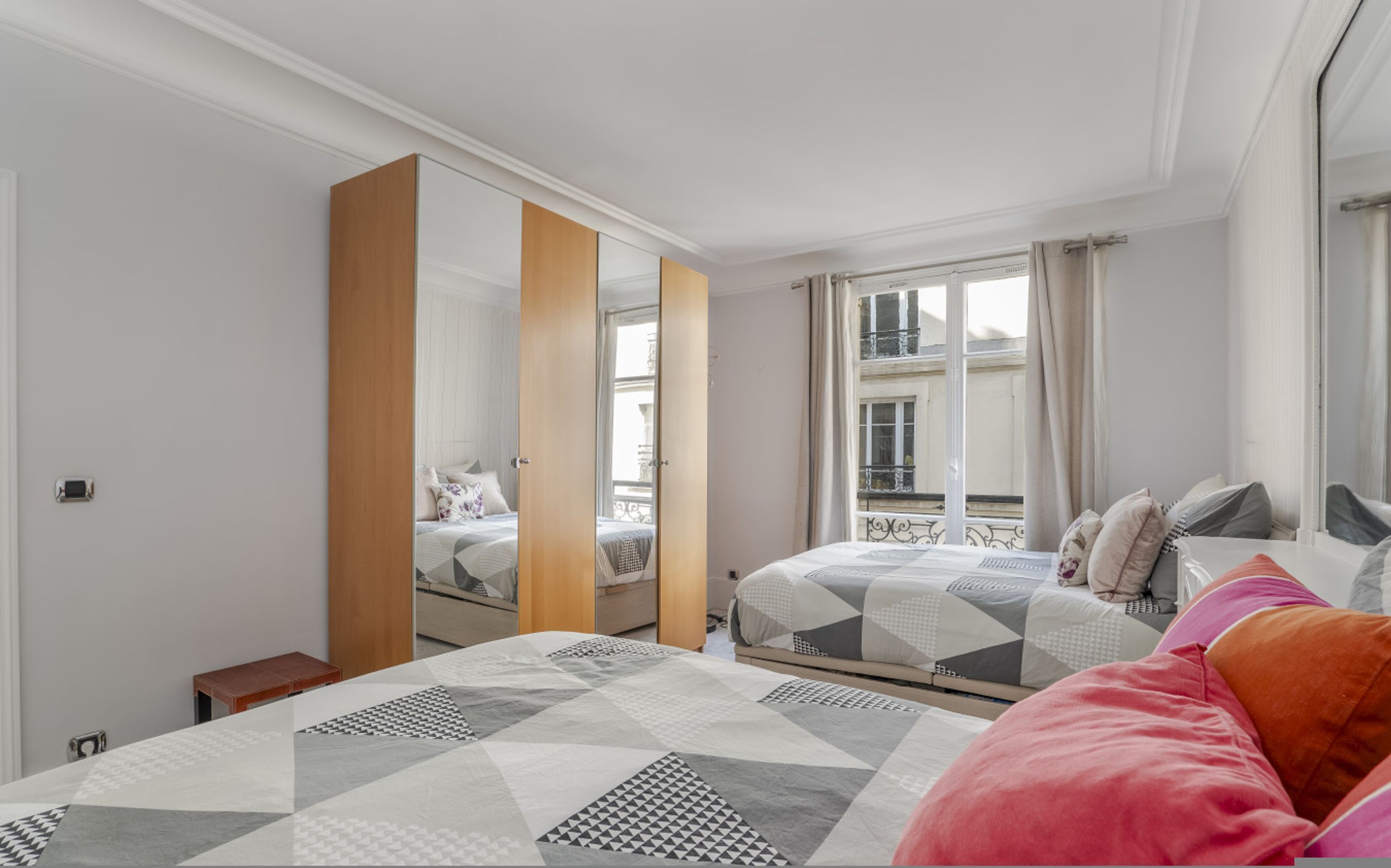 Un dormitorio moderno con dos camas, un espejo grande y una ventana con vistas a edificios.