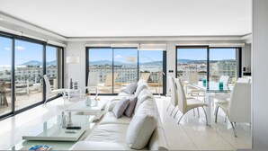 Un soggiorno moderno con un tavolo in vetro, un divano bianco e ampie finestre con vista sulla città.