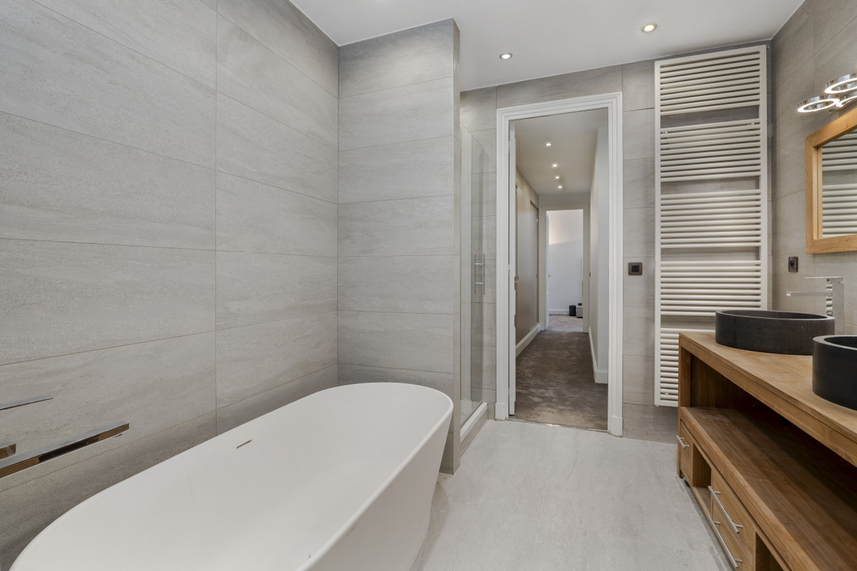 Une salle de bain moderne avec une baignoire sur pieds, un meuble-lavabo en bois doté de deux vasques noires et un grand miroir.