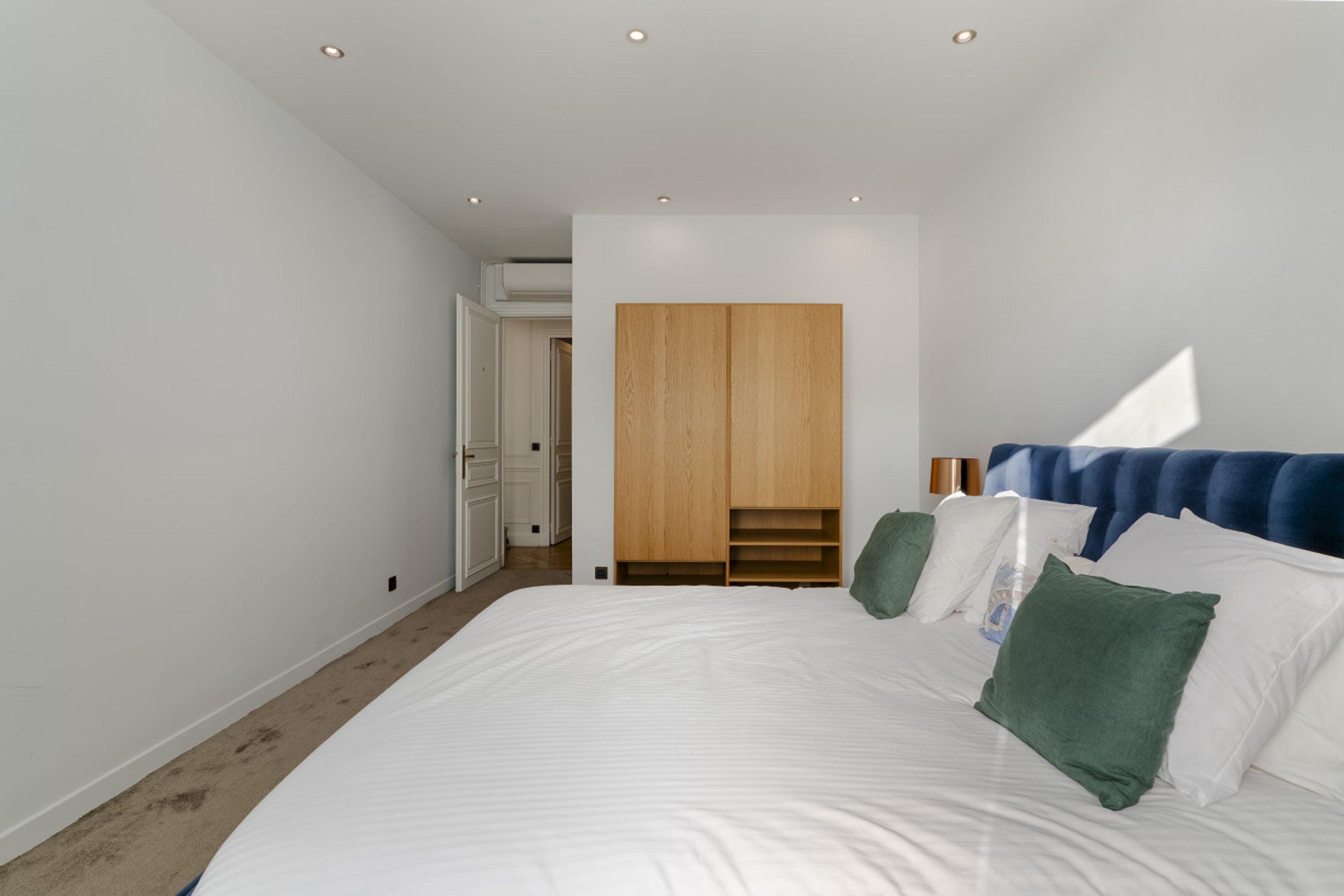 A bedroom with a large bed, a wardrobe, and a door leading to another room.