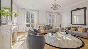 Een ruime woonkamer met een open haard, banken, een salontafel en een grote spiegel.