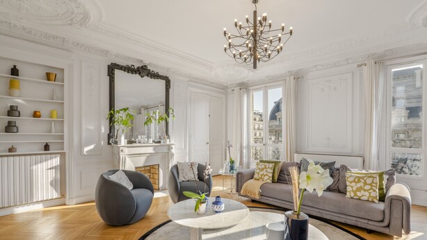 Een ruime woonkamer met een open haard, een grote spiegel en een bank met decoratieve kussens.
