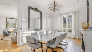 Een ruime eetkamer met een grote witte tafel, moderne stoelen en een weelderige spiegel.