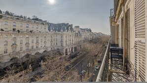 Uitzicht vanaf een balkon op een straat met historische gebouwen, een heldere lucht en een schijnende zon.