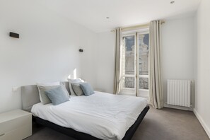 Een moderne slaapkamer met een groot bed, een nachtkastje, een radiator en een raam met gordijnen.