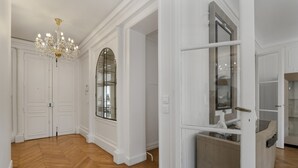 A spacious room with a herringbone wooden floor, white walls, a large arched window, and a chandelier. - Luxury 5 Bed Residence - Opposite Arc de Triomphe (Paris)