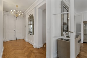 A spacious room with a herringbone wooden floor, white walls, a large arched window, and a chandelier. - Luxury 5 Bed Residence - Opposite Arc de Triomphe (Paris)