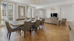 A spacious living area with a large dining table, comfortable seating, a modern kitchen, and a large window offering a view of the city. - Luxury 5 Bed Residence - Opposite Arc de Triomphe (Paris)