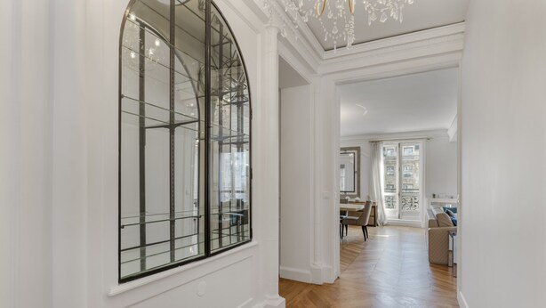 A spacious hallway with a large arched window, wooden flooring, and a view into a dining area. - Luxury 5 Bed Residence - Opposite Arc de Triomphe (Paris)