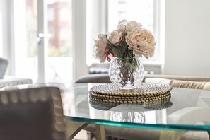 Un tavolo di vetro trasparente con un sottobicchiere intrecciato e un vaso di fiori.