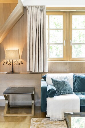 A modern living room with a wooden floor, a sofa with a white throw blanket, a side table with a lamp, and a window with curtains. - Mayfair Home Central AC Huge Terrace (London)